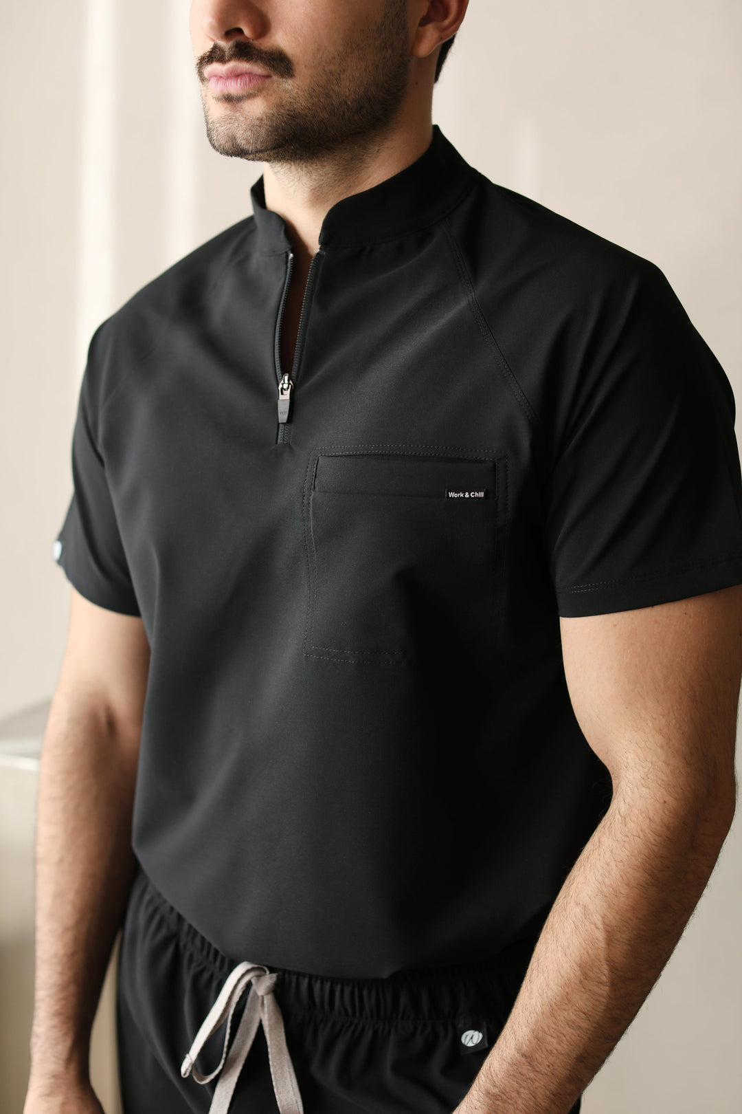 Close-up of a man wearing the Harry Black W&amp;C Shield™ scrub top, highlighting the high collar, front zipper, and chest pocket.