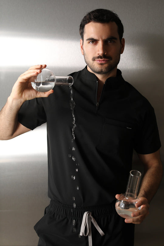 Man wearing the Harry Black W&amp;C Shield™ scrub top while pouring clear liquid from a laboratory flask.
