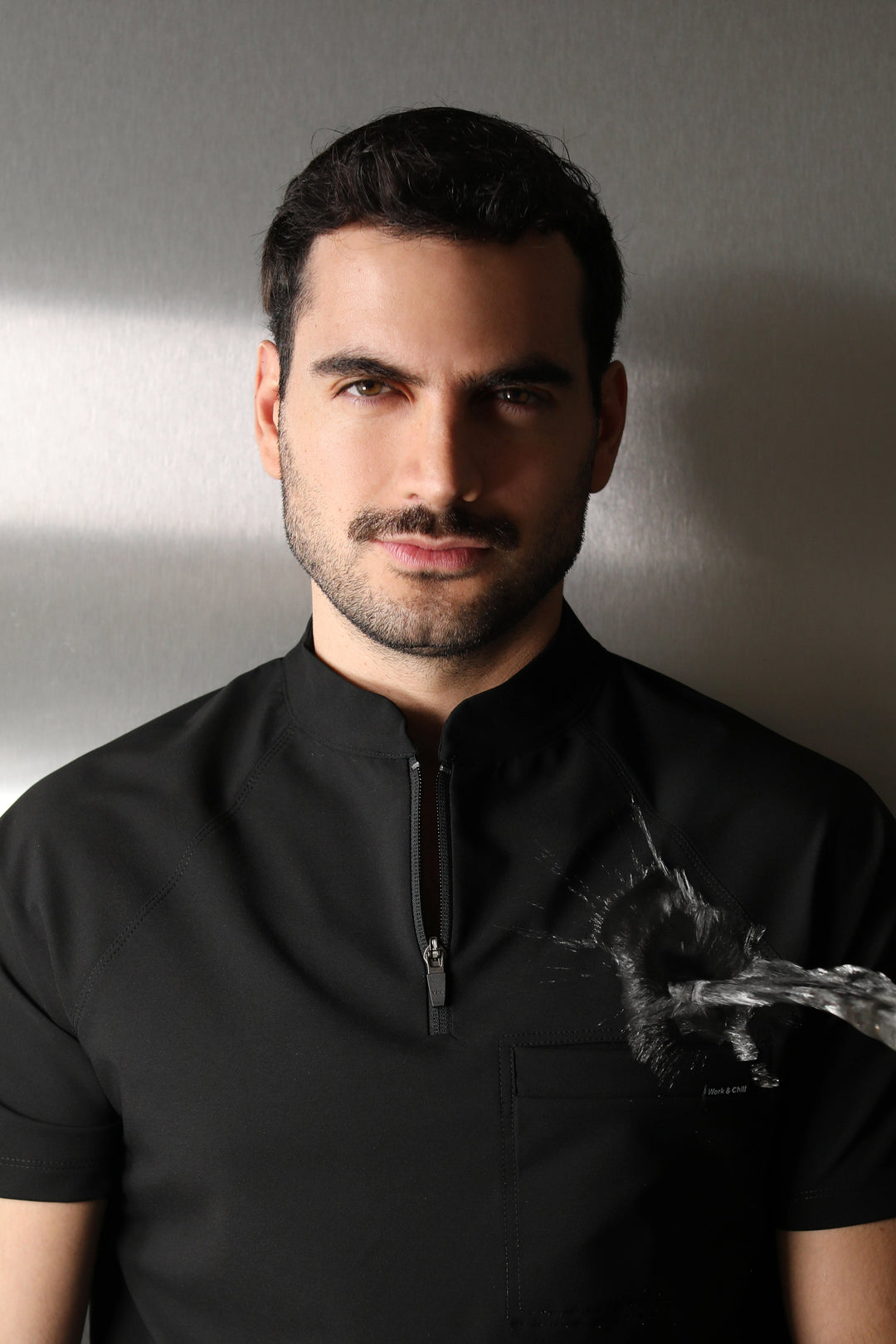 Close-up portrait of a man wearing the Harry Black W&amp;C Shield™ scrub top during a water-repellency demonstration.