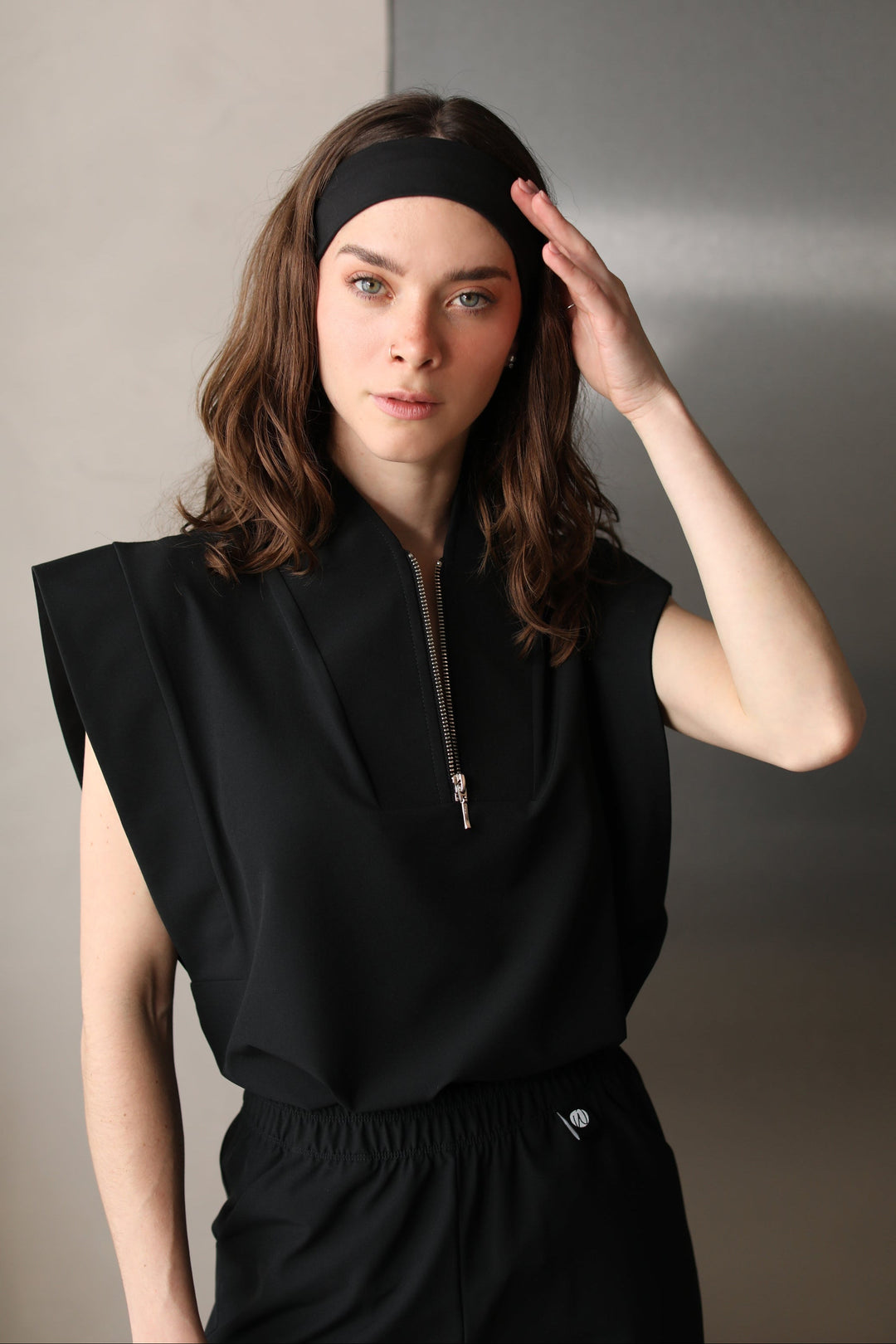 Woman wearing the Kate Black W&amp;C Shield™ scrub top, shown from the waist up with one hand touching her headband.