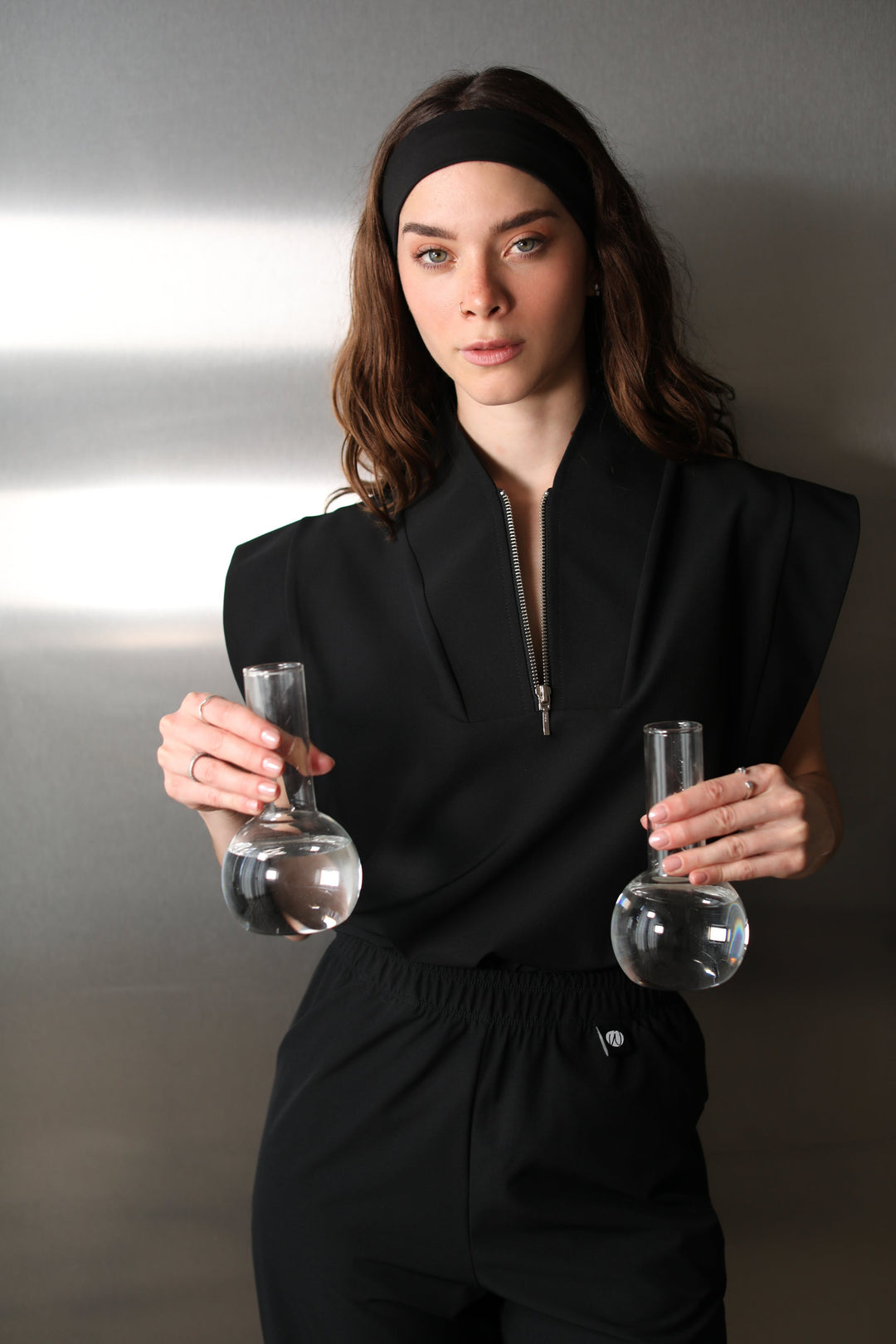 Woman wearing the Kate Black W&amp;C Shield™ scrub top while holding two laboratory flasks filled with clear liquid.